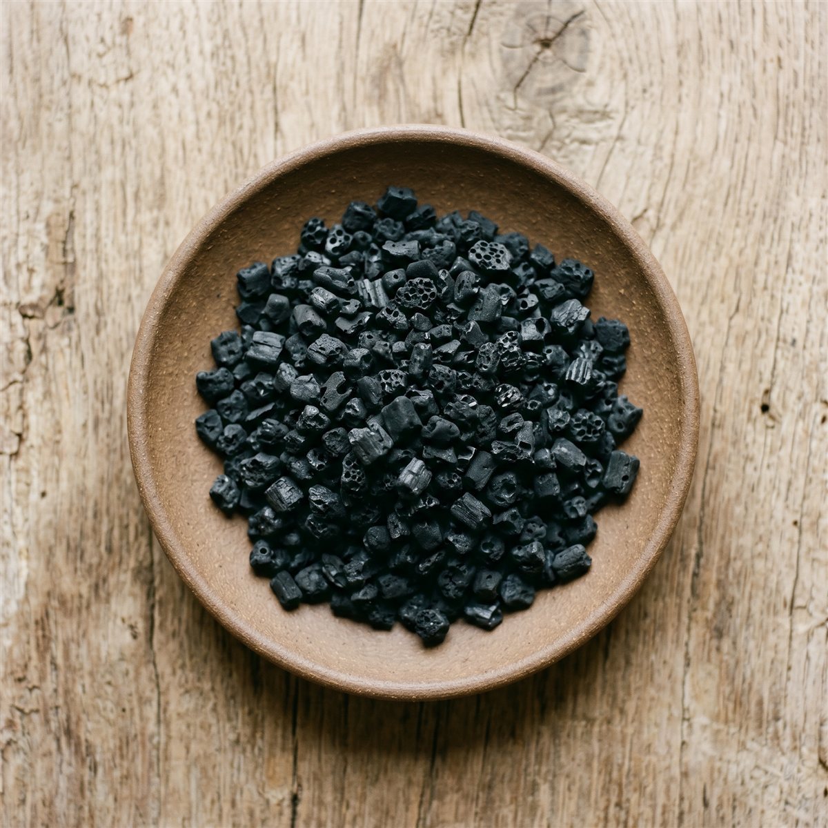 Fine black biochar in a bowl on a weathered wood surface