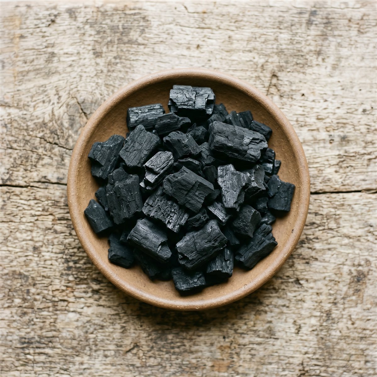 Horticultural charcoal chunks in a ceramic bowl on a weathered wood surface