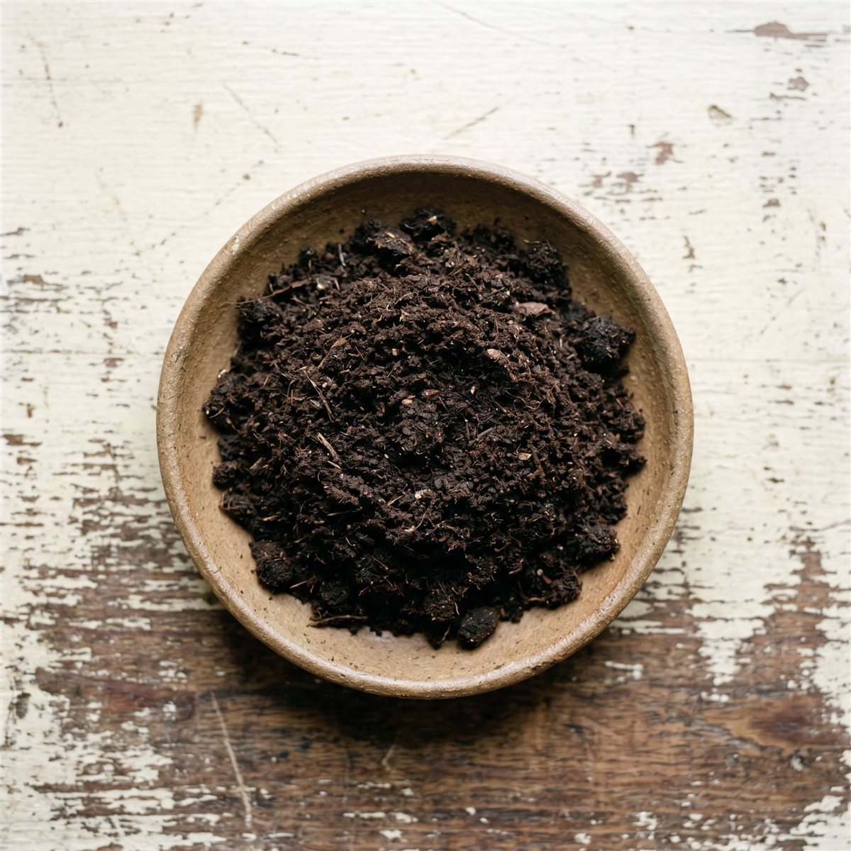 Fine brown milled peat moss in a bowl on a weathered wood surface