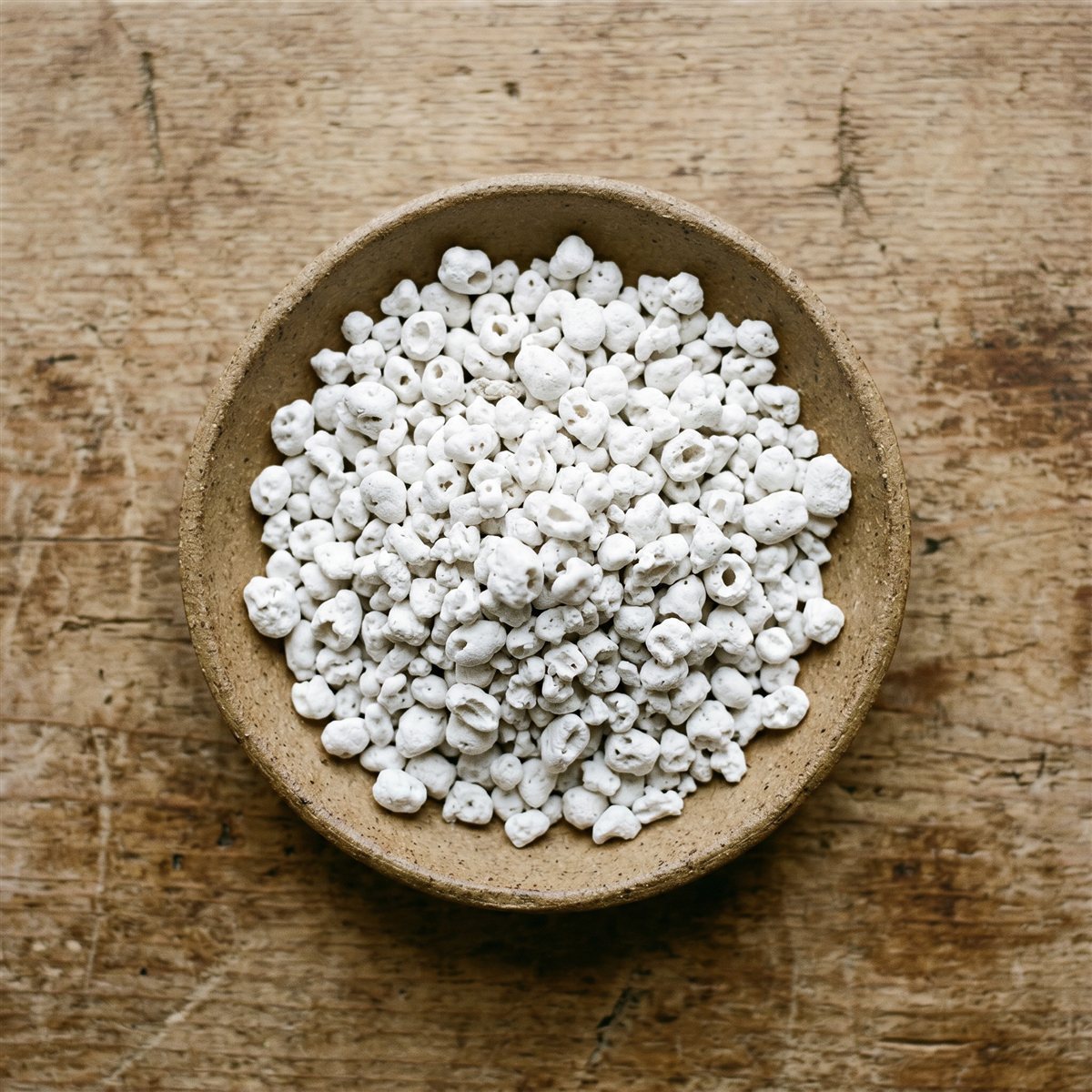 Coarse white perlite particles in a bowl on a weathered wood surface