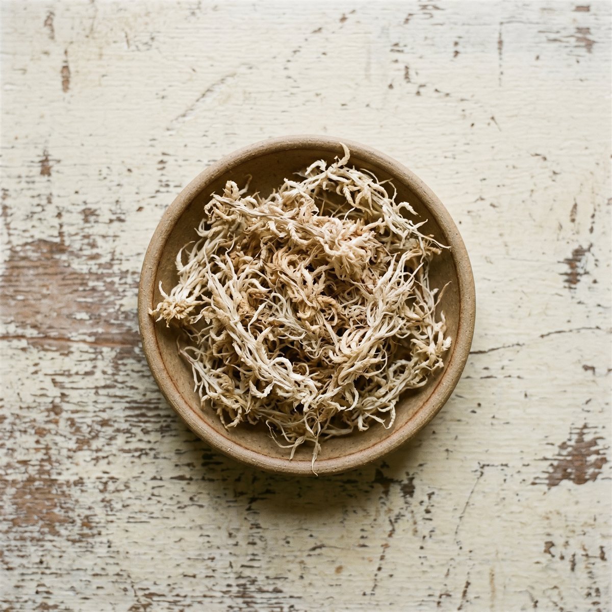 Dried long-fiber sphagnum moss in a bowl on a weathered wood surface