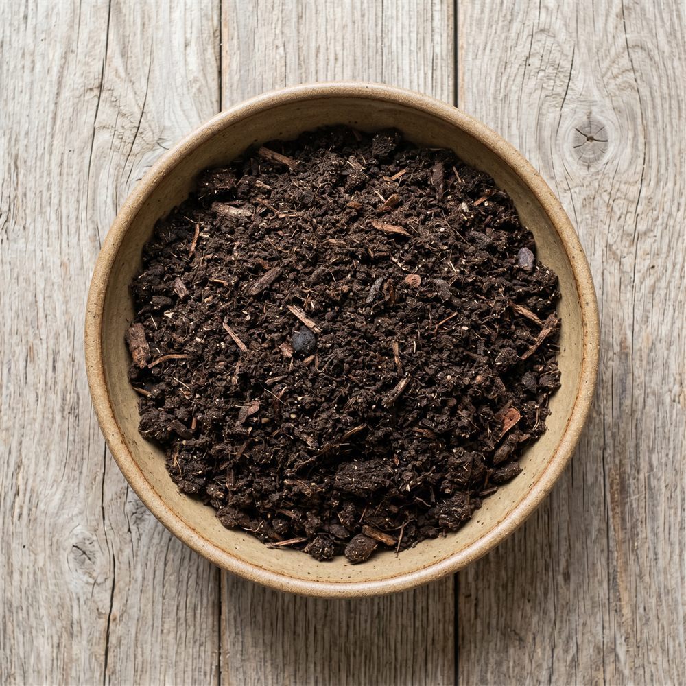 Dark bagged potting soil in a bowl on a weathered wood surface