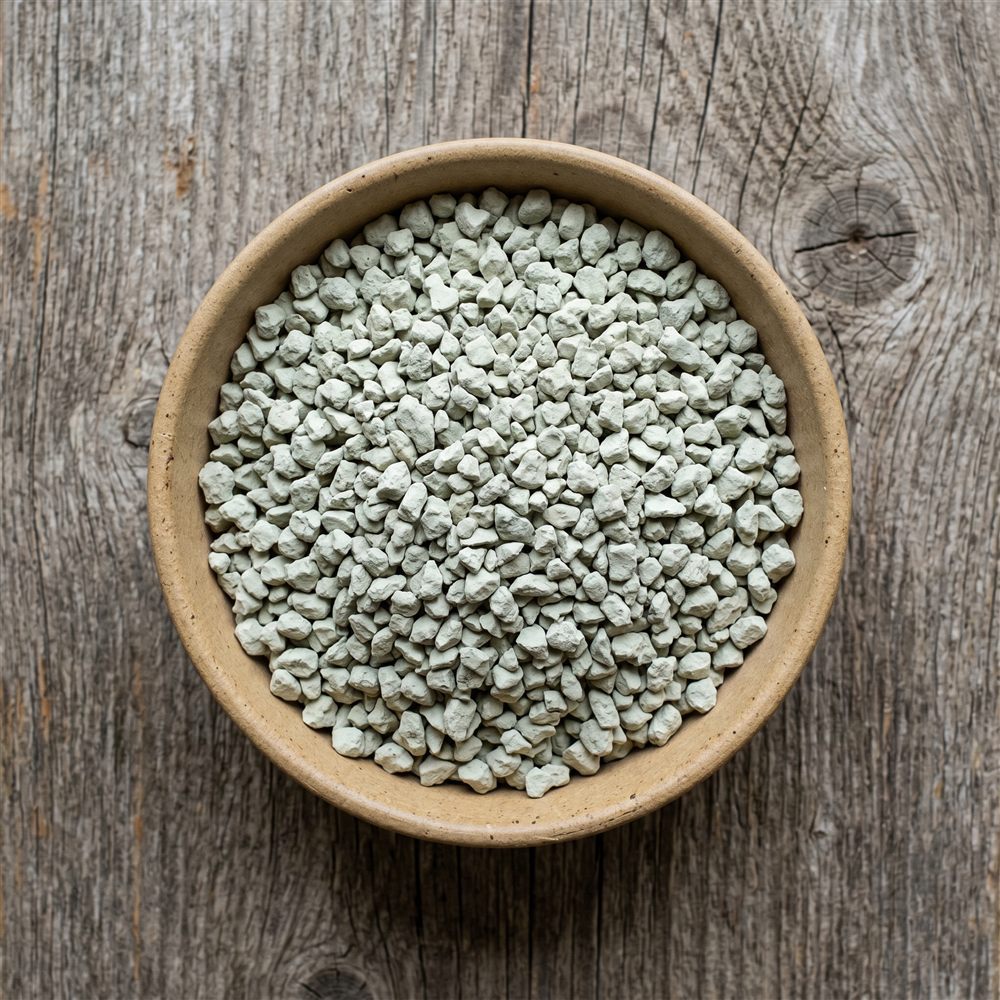 Pale green-grey zeolite granules in a bowl on a weathered wood surface